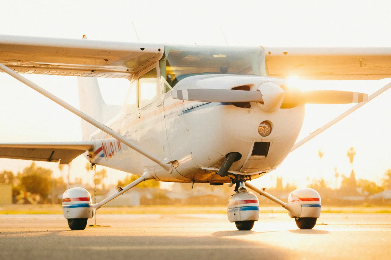 A white high-wing aircraft parked on the apron in warm evening light, with its propeller and landing gear in view.